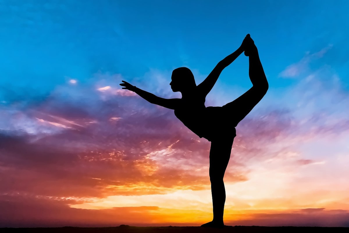 A silhouetted figure of a woman doing a yoga pose in front of a sunset