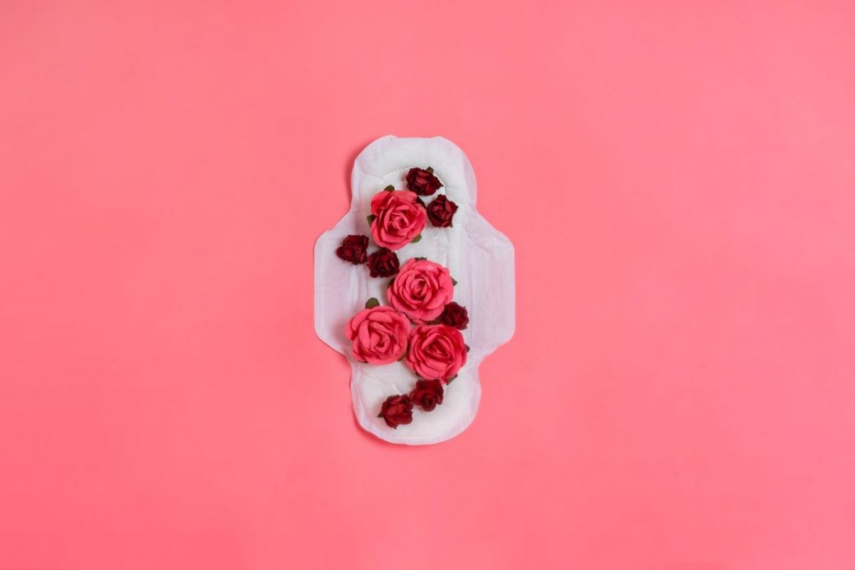 Four big pink roses and seven small red roses laid on a sanitary pad on a pink background