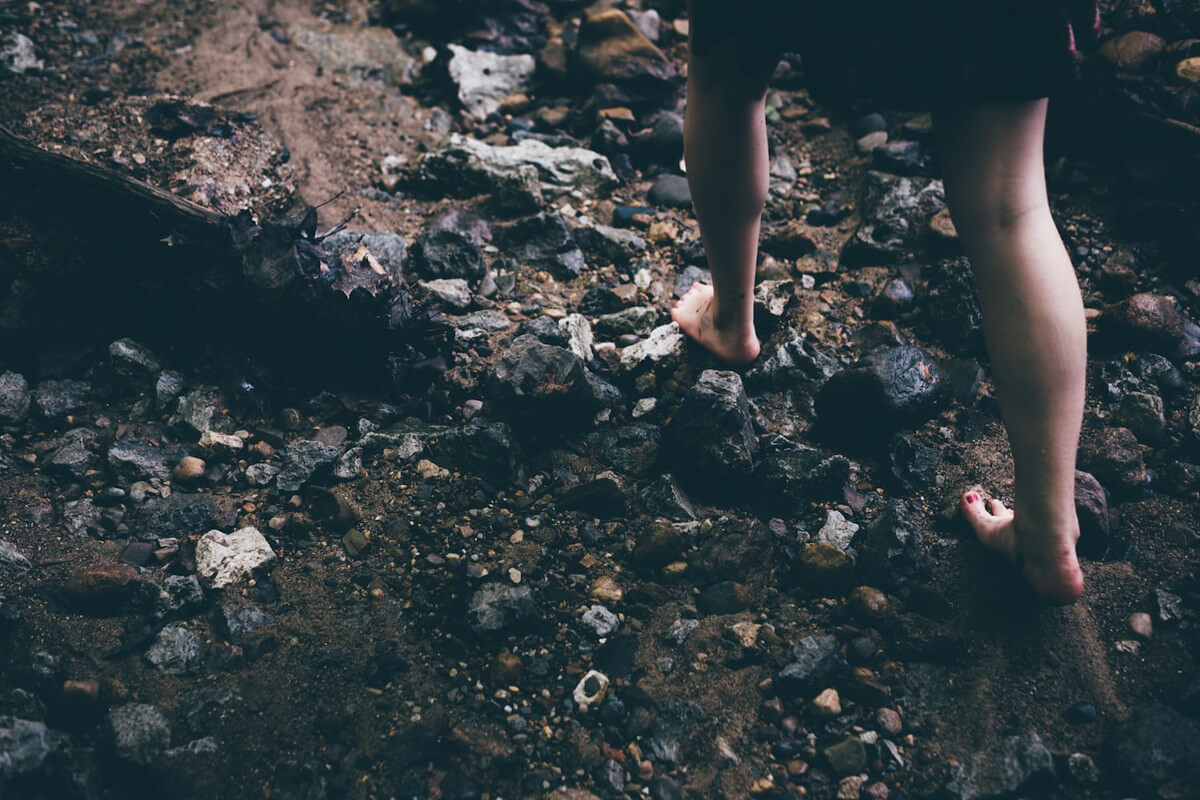 A pair of bare feet of a woman walking on rocky terrain